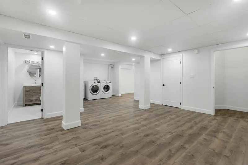 Finished basement with white walls, vinyl plank flooring and a laundry area