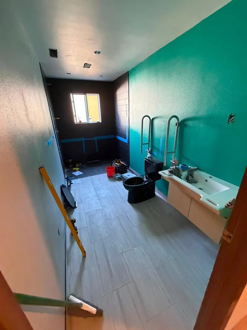Bathroom conversion in progress: new gray floor tile, teal walls, grab bars and a wall-hung vanity being fitted