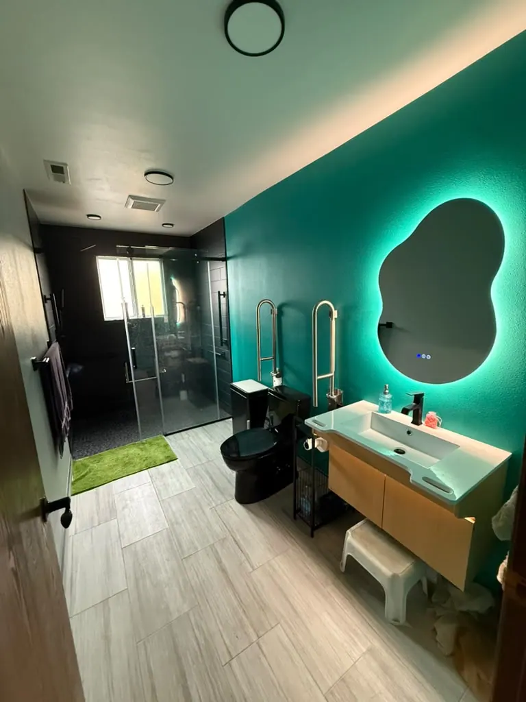 Finished accessible bathroom with a teal wall, a backlit mirror, a floating wood vanity and a glass walk-in shower