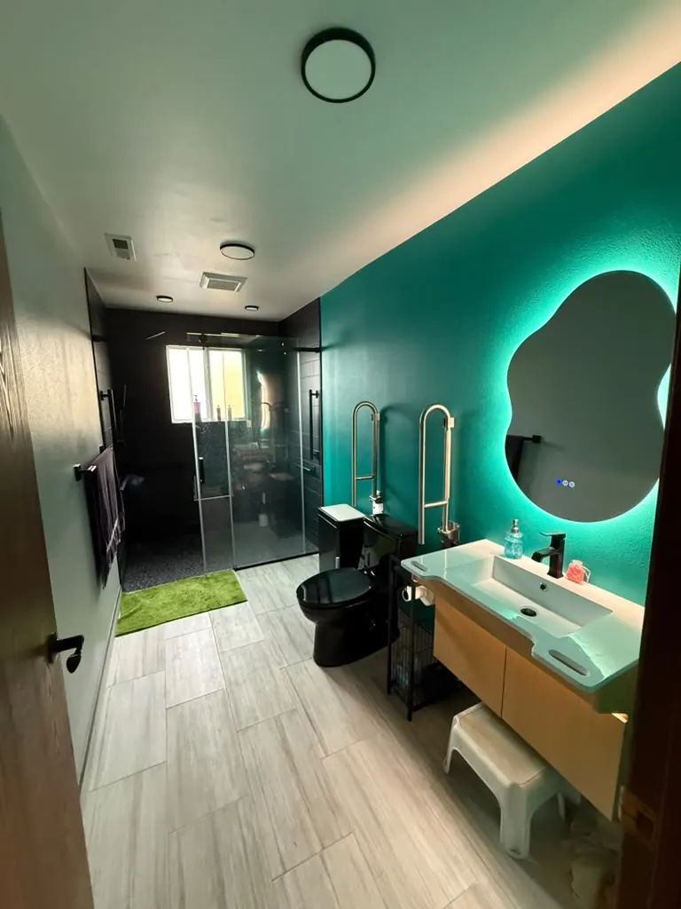 Accessible bathroom with a teal accent wall, a floating wood vanity, grab bars and a dark-tiled shower