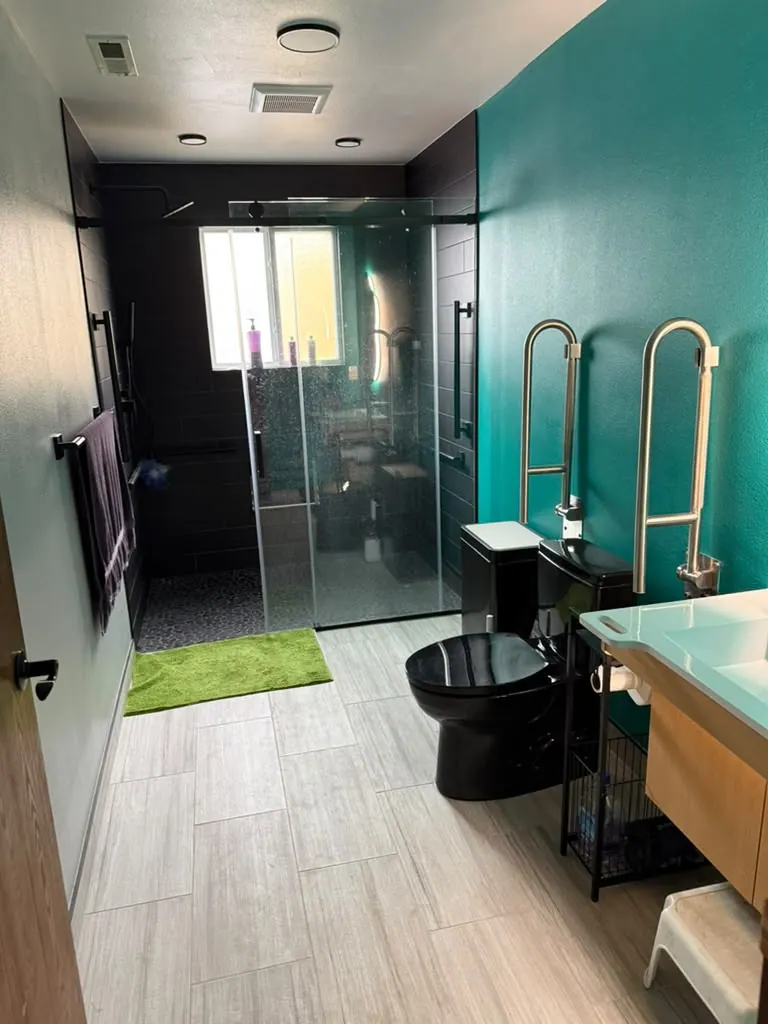 After: Converted full bathroom with a glass shower, a teal accent wall, a black toilet and grab bars