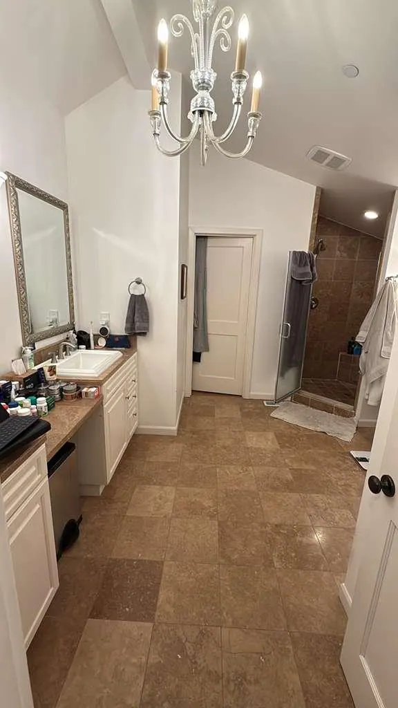 Before: The vanity wall before the remodel, with white cabinets, a brown countertop and travertine floor tile