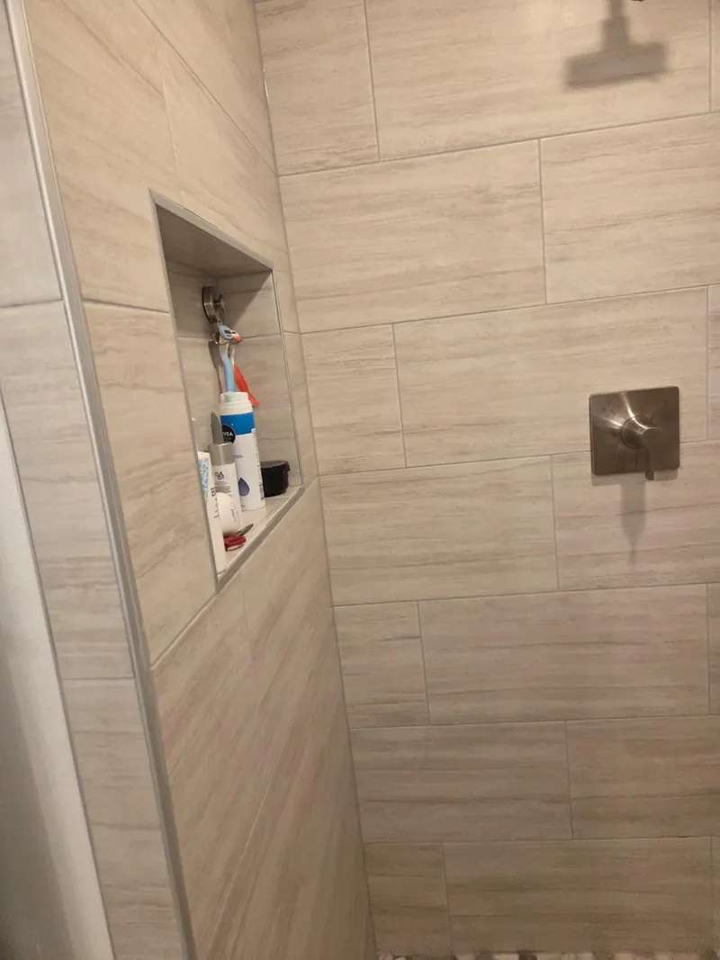 Close-up of new shower wall tile with a recessed storage niche and a brushed-nickel shower control