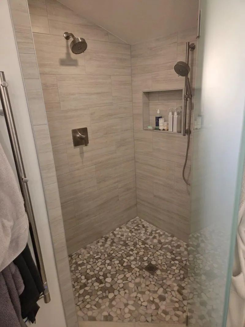 Finished shower seen through the glass, with gray wall tile, a niche and a pebble mosaic floor