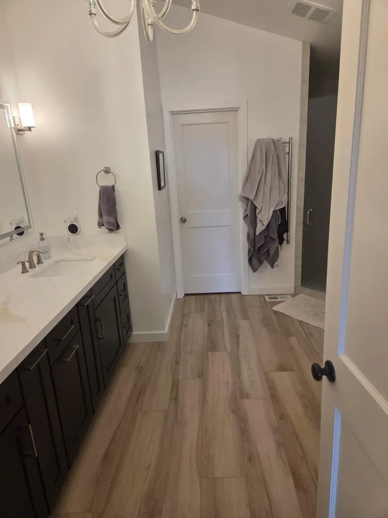 After: Remodeled bathroom with a dark vanity, a white countertop and wood-look plank flooring