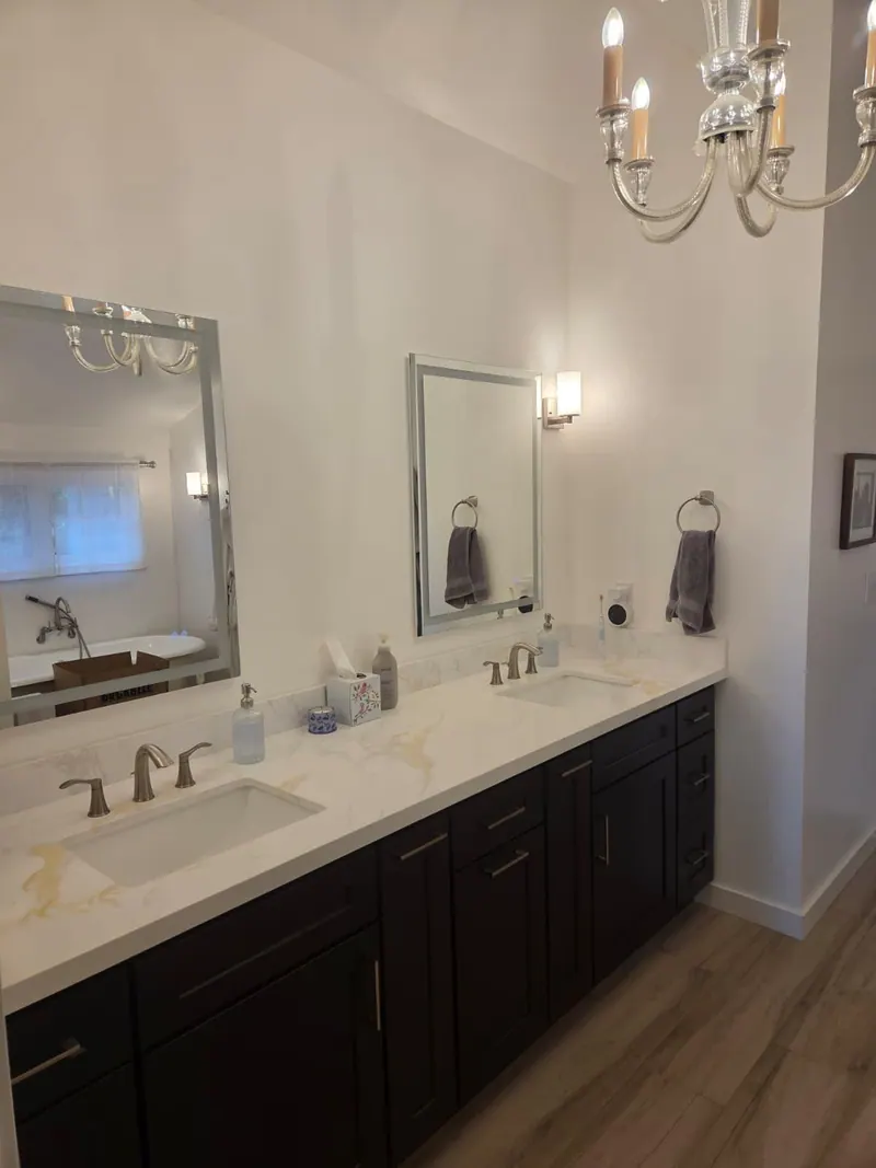 After: New double vanity with dark cabinets, a white veined countertop, framed mirrors and wall sconces