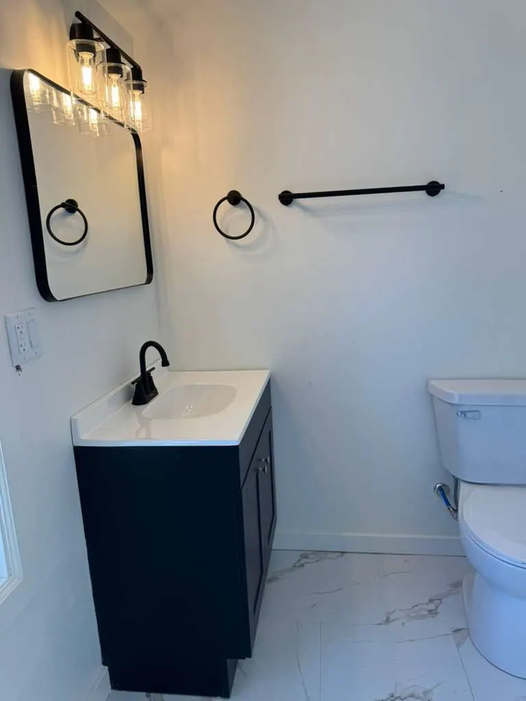 Small remodeled bathroom with a navy vanity, black fixtures and marble-look floor tile