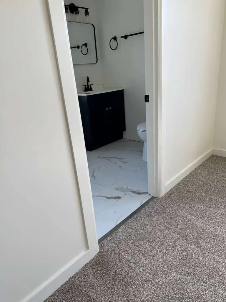 Doorway view into a small bathroom with a navy vanity and marble-look tile next to new gray carpet
