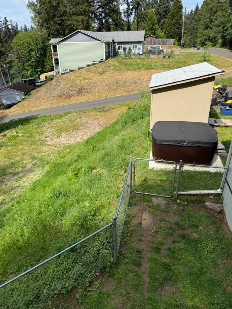 Before: The yard before the deck was built: a grass slope around a hot tub and a shed, behind a chain-link fence