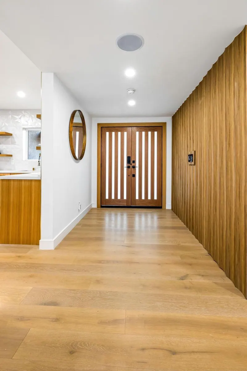 Wide-plank wood flooring running down an entry hall with wood wall paneling and a double front door
