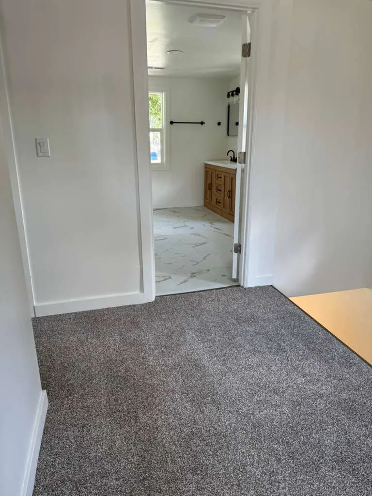 Gray carpeted landing meeting marble-look bathroom tile at the doorway