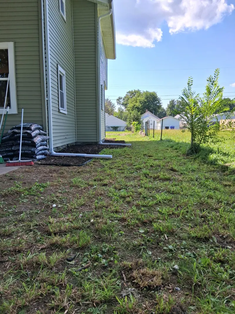 Side of the house with sage siding, white downspouts and freshly mulched beds