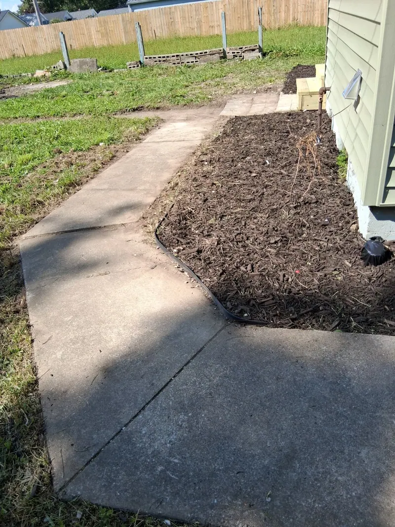Concrete walkway curving past a new mulched bed along the sage siding