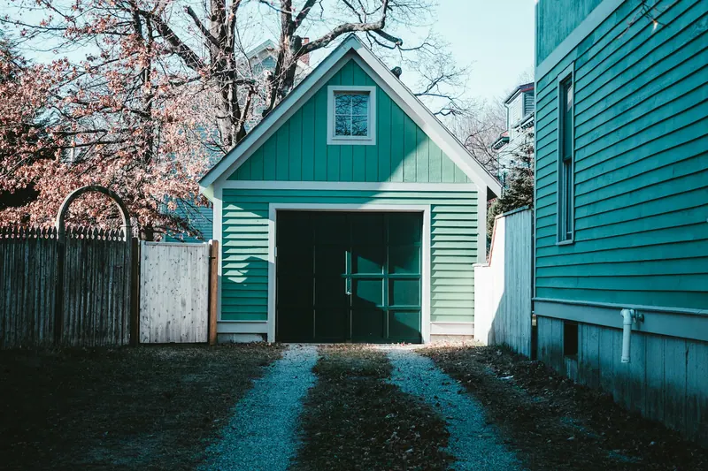 Teal detached garage with a dark door at the end of a driveway