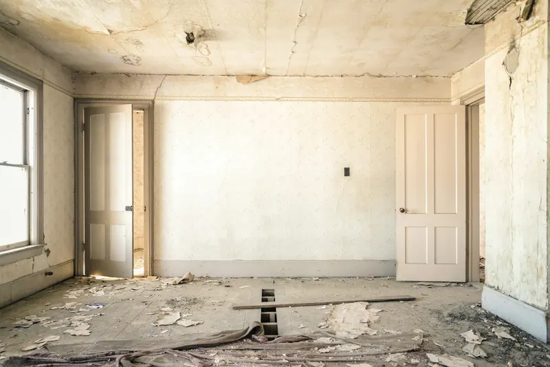 Gutted room with peeling walls and damaged flooring before renovation