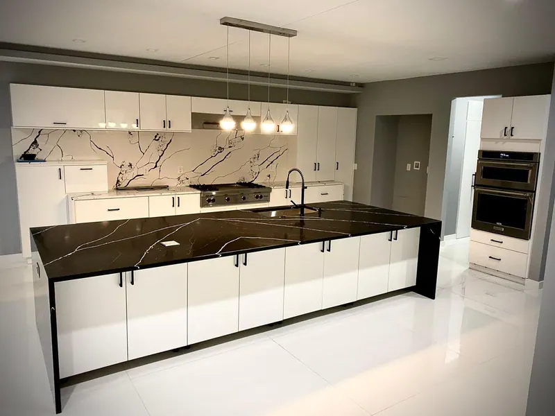 Kitchen with white cabinets, a black waterfall island, a veined stone backsplash and pendant lights