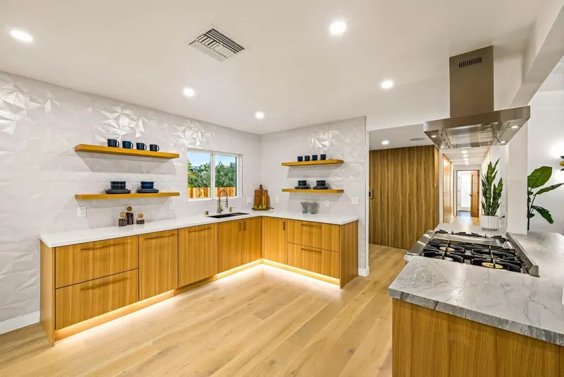 L-shaped wood kitchen with white countertops, floating shelves and lit toe kicks