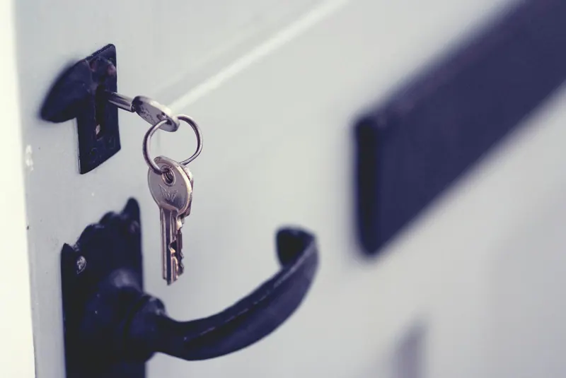 Keys in a lock on a white door with a black handle