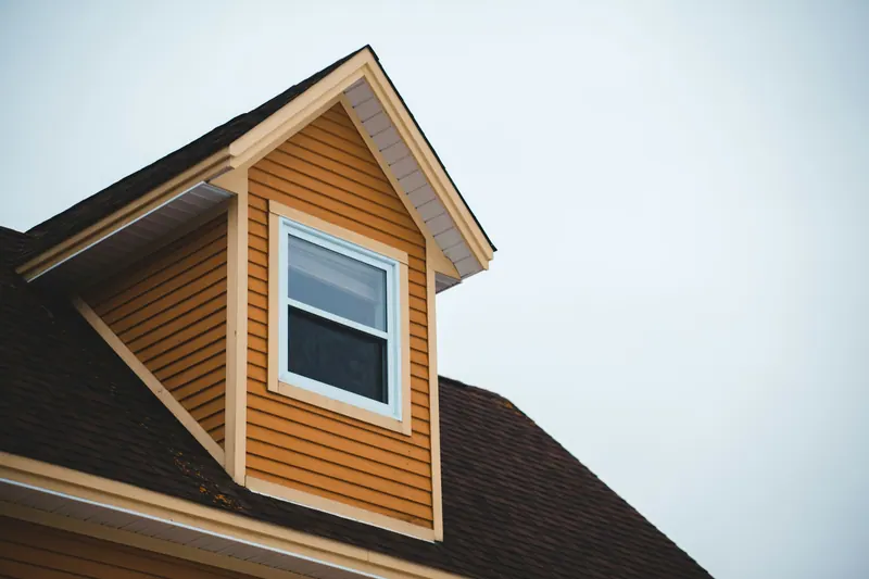 Dormer clad in wood-tone siding on a shingle roof