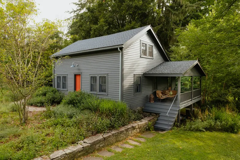 Small gray-sided house with a red door and a garden